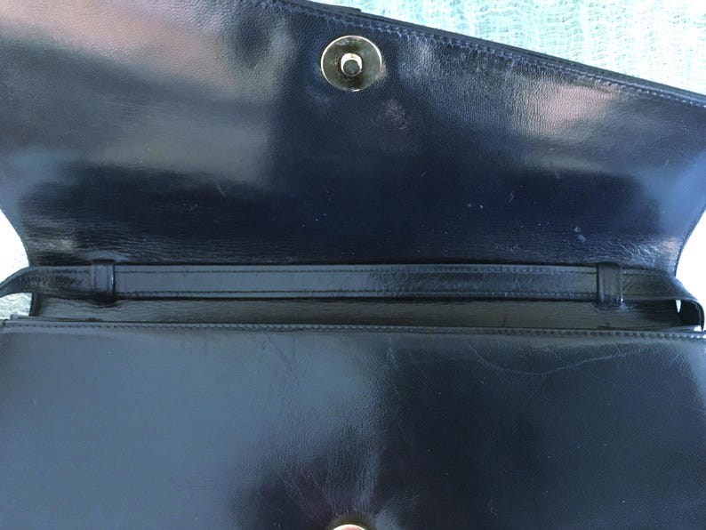 May include: A navy blue leather handbag with a flap closure and a gold-colored clasp. The interior features a strap and a smooth, glossy finish. The bag is open, revealing the inside.