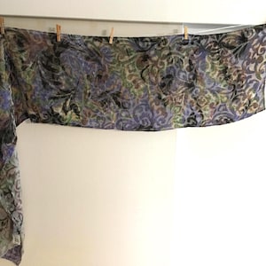 Puede incluir: Una taza de cerámica blanca con asa negra y el texto "But First, Coffee" en negrita negra. La taza se encuentra sobre un fondo borroso, sugiriendo un ambiente acogedor.