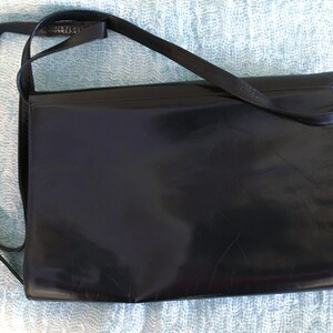 May include: A black leather crossbody bag with a rectangular shape. The bag has a long, thin strap and a gold-colored buckle. The leather appears shiny and smooth, with a subtle sheen.
