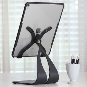 May include: A black iPad stand with a curved base and a swivel arm to hold a tablet. The stand is made of metal and has a sleek, modern design.