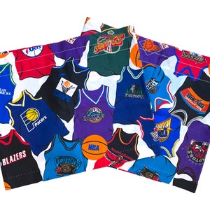 May include: A white fabric with a patchwork design of various NBA team jerseys. The jerseys feature different team logos and colors, including the Dallas Mavericks, Indiana Pacers, Cleveland Cavaliers, Atlanta Hawks, and more.