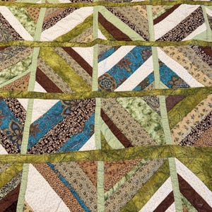 May include: A patchwork quilt with a repeating pattern of diagonal stripes in various colors and patterns. The quilt features stripes of brown, green, blue, and white fabrics. The quilt is bordered with a darker green fabric.