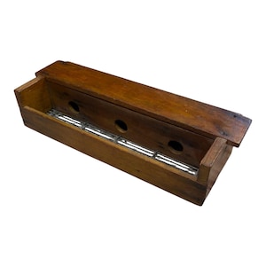 May include: A rectangular wooden box with a hinged lid. The box is made of dark brown wood and features three circular holes and a metal grate. The box is open, revealing the interior.