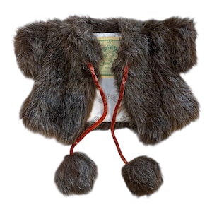 May include: A brown fur bolero jacket with short sleeves and a plush texture. The jacket features red velvet ties with matching pom-poms. The interior lining is white with a patterned design and a label.