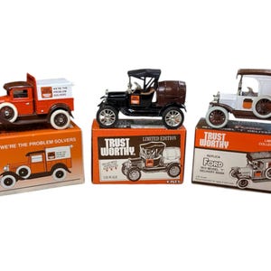 May include: Three vintage Ford Model T delivery trucks, each in a different color scheme, are displayed in their original boxes. The boxes are orange and feature the Trustworthy Hardware Stores logo and the text "We're the problem solvers".
