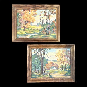 May include: Two framed landscape paintings. The top painting depicts a stream winding through a field with trees in autumn colors. The bottom painting shows a road leading to a white house, with trees and a fence. Both paintings are in wooden frames.