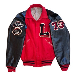 May include: Red and black varsity jacket with leather sleeves. The jacket has a large "L" on the front and the number "73" on the right sleeve. The sleeves have patches that say "Convention All Dist 73" and "All Dist Tackle 1-AAA 73".