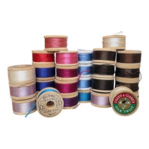 May include: A collection of vintage wooden spools wound with colorful silk thread. The spools feature printed labels including Belding Corticelli 10 YDS Size D Pure Silk Twist and Coats & Clark's Silk Twist. The threads are in shades of red, pink, blue, purple, brown, and white.