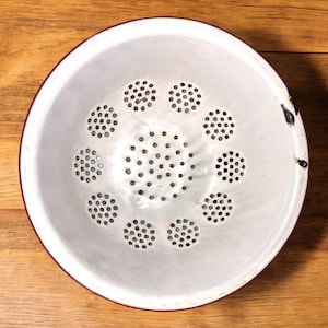 May include: White enamel colander with a red rim and a circular pattern of holes.