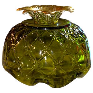 May include: A green glass pineapple-shaped jar with a gold metal top. The jar has a textured surface that resembles a pineapple.