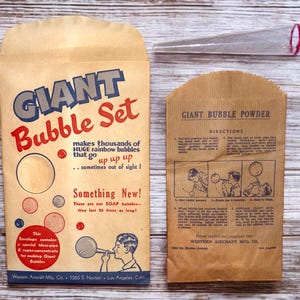 May include: A vintage brown paper envelope with the text "GIANT Bubble Set" in blue and red lettering. The envelope contains a bubble blowing kit that makes "thousands of HUGE rainbow bubbles that go up up up... sometimes out of sight!" The envelope also includes the text "Something New! There are not SOAP bubbles... they last 20 times as long!" The envelope is next to a smaller brown paper envelope with the text "GIANT BUBBLE POWDER" in blue lettering. The smaller envelope has instructions for making giant bubbles and a copyright notice for Western Aircraft Mfg. Co.