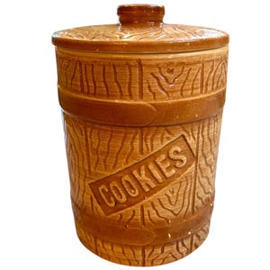 May include: A brown ceramic cookie jar with a woodgrain design and the word "COOKIES" on the front.