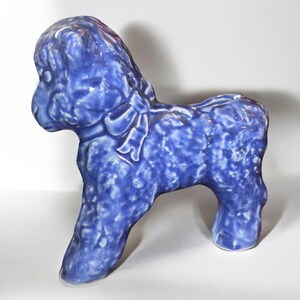 May include: A blue ceramic figurine of a sheep with a textured surface. The sheep has a bow on its neck.
