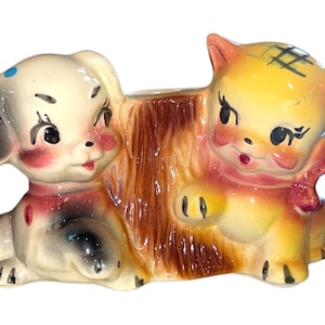 May include: A vintage ceramic planter featuring a cartoon dog and cat. The dog is black and white with blue spots and a red collar. The cat is yellow with a pink bow and brown stripes. The planter is brown and has a tree trunk design.