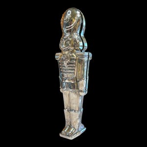 May include: A silver-colored nutcracker in the shape of a toy soldier. The nutcracker has a detailed face, uniform, and hat. The design is a classic holiday decoration, perfect for cracking nuts during the festive season.