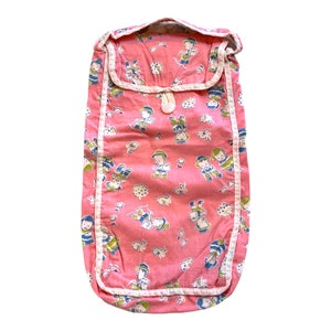 May include: A vintage pink baby sleeping bag with a whimsical pattern of children, animals, and cookies. The bag has a rectangular shape with a flap closure and white trim. The fabric is a soft, printed cotton.