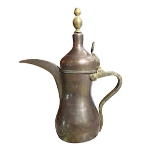 May include: A traditional brass coffee pot with a rounded body and a spout. The pot has a decorative handle and a small finial on the lid.