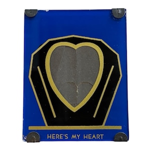 May include: A blue picture frame with a heart-shaped opening. The frame has a black and gold heart design, with the text "HERE'S MY HEART" at the bottom. Metal corner pieces secure the frame.