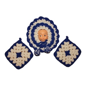 May include: A set of three crocheted items in white and blue. The center item is a doll's bonnet with a plastic doll head inside. The other two items are square crocheted pads.
