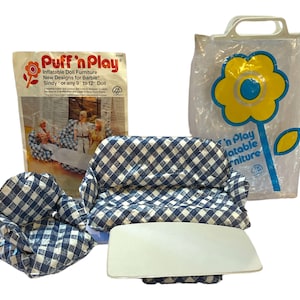 May include: A set of blue and white gingham patterned inflatable doll furniture, including a sofa, two chairs, and a table. The furniture is packaged in a clear plastic bag with a yellow flower design and the text 'Puff 'n Play Inflatable Furniture'.