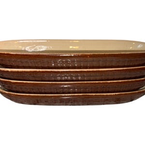 May include: A stack of five brown ceramic plates with a textured, ridged design on the sides. The top plate is a light tan color. The plates are oval-shaped and appear to be for serving food.