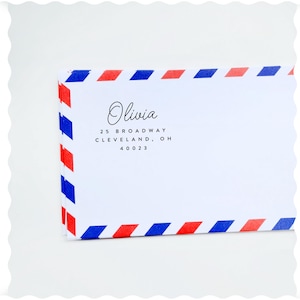 Op de afbeelding: Een witte envelop met rode en blauwe strepen. De envelop heeft de naam "Olivia" en het adres "25 Broadway, Cleveland, OH 40023" erop gedrukt.