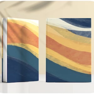 May include: Two views of a hardcover journal with a colorful abstract design. The cover features a pattern of wavy lines in shades of blue, yellow, orange, and white. The text "G.V.A." is printed in black on the front cover.