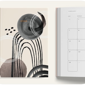 May include: A beige planner with a black and white abstract design on the cover. The cover features a large circle with a black and white design, a smaller circle with a brown and white design, and a black and white abstract design. The planner is open to the month of February.
