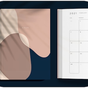 May include: A closed, pink and blue planner with the word "GVAN" on the cover. The planner is open to February 2021.