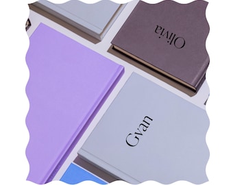 Op de afbeelding: Vijf hardcover-journaals met verschillende gekleurde omslagen en gepersonaliseerde namen: Olivia, Gyan en drie anderen.