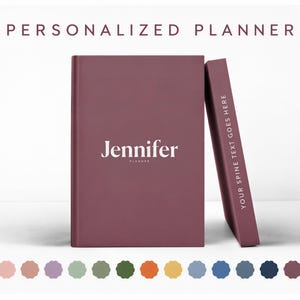 May include: A dark mauve personalised planner with the name Jennifer printed in white on the front cover. A second planner stands vertically next to it, displaying the text YOUR SPINE TEXT GOES HERE. A row of sixteen coloured circles is below.