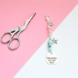 May include: A silver charm bracelet with pink and blue beads, a silver starfish charm, and a silver charm with the text "Dreaming of the Sea".