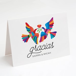 May include: White folded card featuring two colorful birds with rainbow wings, holding a heart and sprig. The word "gracias" is written in cursive, with "SIERRA & MICAH" below.
