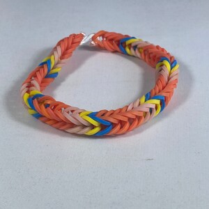 May include: A colorful bracelet made of woven rubber bands. The bracelet features a pattern of orange, pink, yellow, and blue bands. The clasp is silver. This handmade accessory is suitable for all ages.