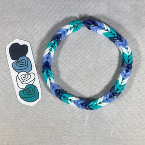 May include: A handmade bracelet with a woven design, featuring a mix of blue, white, and teal rubber bands. Next to the bracelet is a sticker with four heart-shaped designs in shades of blue and teal.