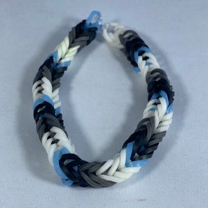May include: A braided bracelet made with black, white, and light blue rubber bands.