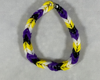 May include: A purple, black and white rubber band bracelet. The bracelet is made of multiple strands of rubber bands that are woven together.