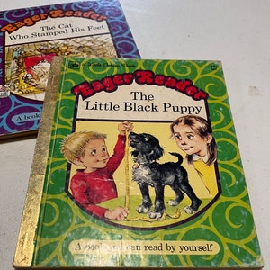 May include: Two vintage children's books. One is titled "Eager Reader: The Little Black Puppy" with a green cover and illustrations of a boy, girl, and puppy. The other book is titled "Eager Reader: The Cat Who Stamped His Feet".