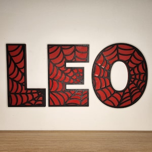 May include: Black wooden letters spelling "LEO" with a red spiderweb design.