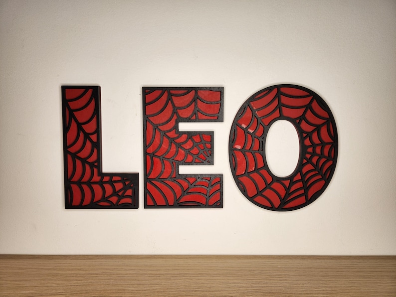 May include: Black wooden letters spelling "LEO" with a red spiderweb design.