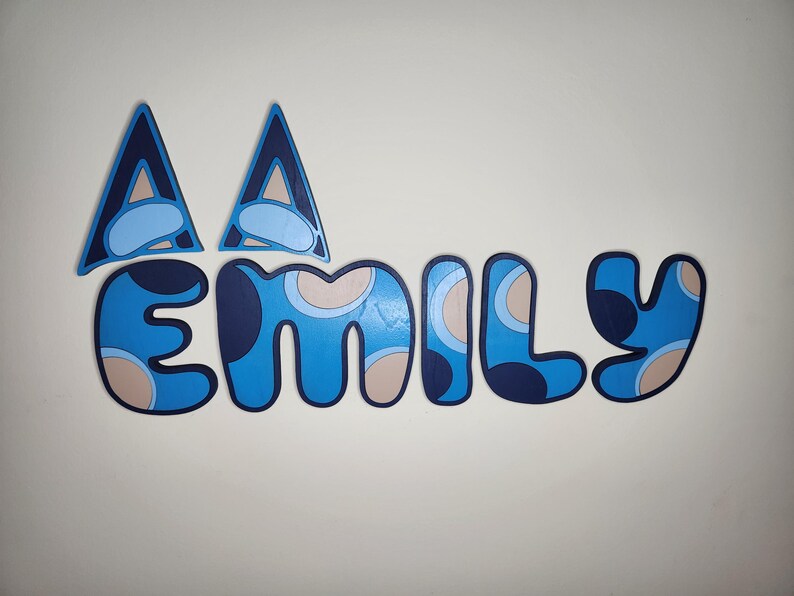 May include: Blue and beige patterned letters spelling out the name "Emily" with two blue and beige triangles above the letters.