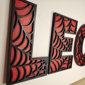 May include: Black and red wooden letters spelling out the name "LEO" with a spiderweb design.