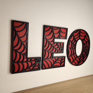 May include: Black wooden letters spelling "LEO" with a red spiderweb design.