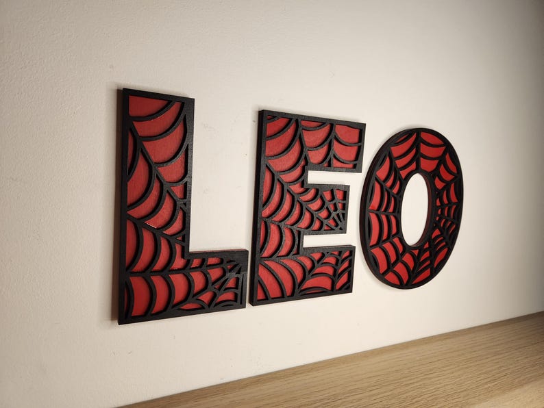 May include: Black wooden letters spelling "LEO" with a red spiderweb design.