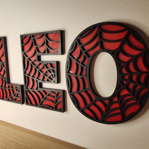May include: Black wooden letters spelling "LEO" with a red spiderweb design.