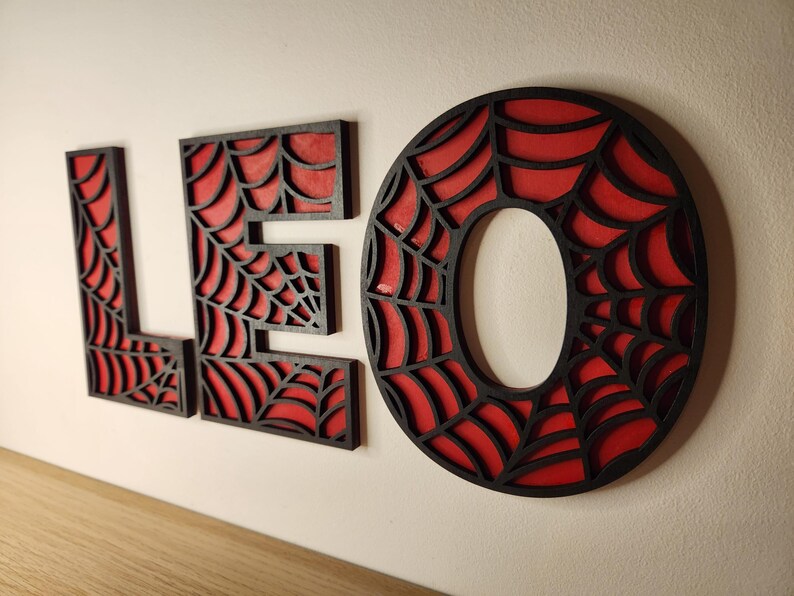 May include: Black wooden letters spelling "LEO" with a red spiderweb design.