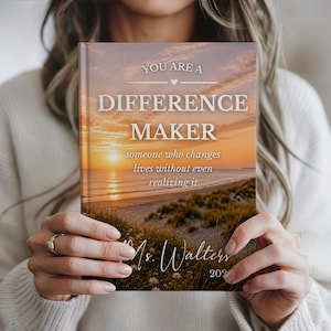 May include: A hardback journal featuring a sunset beach scene. The cover displays the text "YOU ARE A DIFFERENCE MAKER" and the phrase "someone who changes lives without even realising it." Below is the name "Ms. Walters" and the year "202".