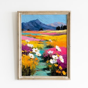 May include: A framed oil painting featuring a vibrant landscape with a field of yellow, pink, and white flowers in the foreground. A path winds through the colorful meadow toward distant blue mountains under a clear light blue sky.