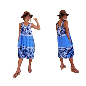 Op de afbeelding: Een blauwe en witte tie-dye maxi-jurk met een ronde hals en zonder mouwen. De jurk heeft een losse pasvorm en heeft twee zakken aan de zijkanten. Het model draagt ​​een bruine hoed en bruine sandalen.