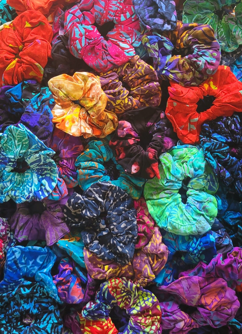 May include: A close-up of a variety of colorful hair scrunchies made from fabric with different patterns. The scrunchies are arranged in a pile, showing off their vibrant colors and designs.